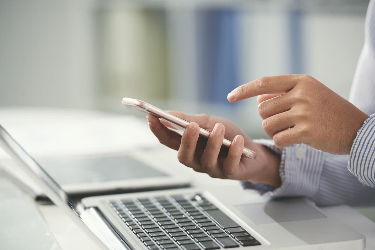 Person using phone with laptop in the background